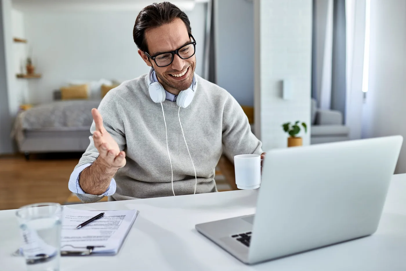 young-happy-businessman-drinking-coffee-using-computer-while-having-video-conference-home-