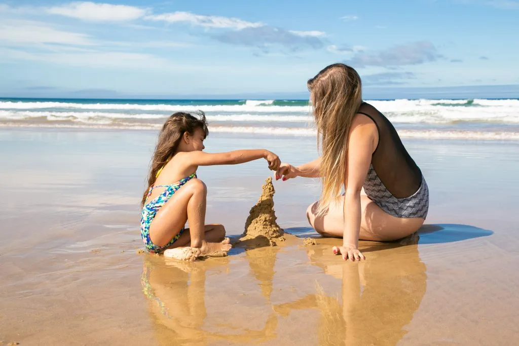 little-girl-her-mom-building-sandcastle-beach-sitting-wet-sand-enjoying-vacation-sea-1024x